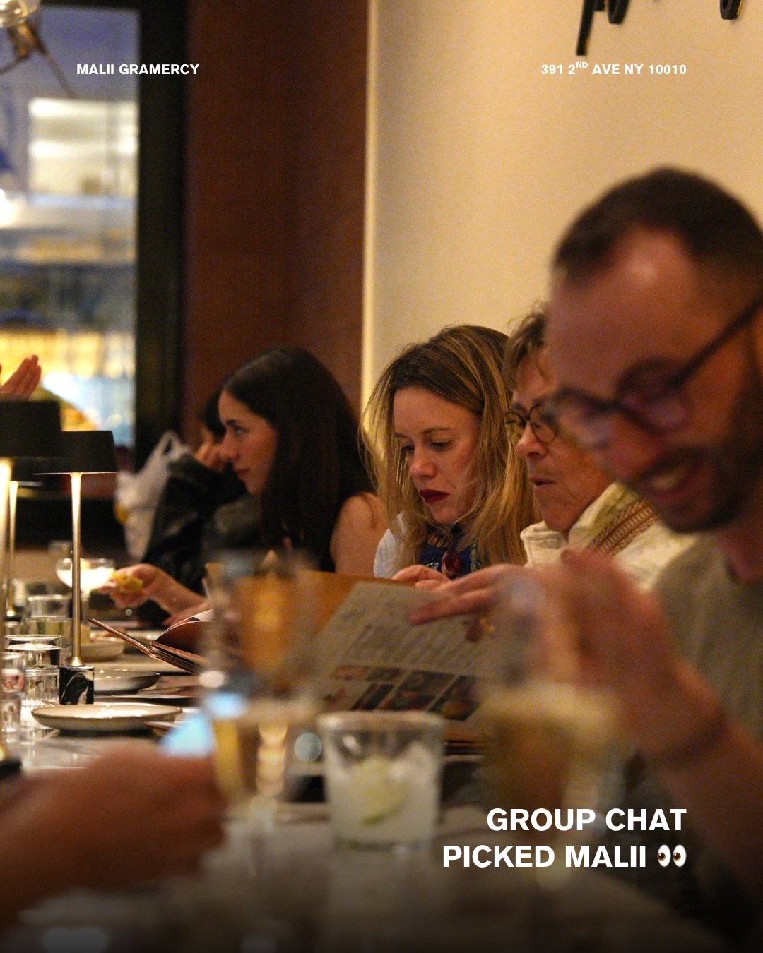 Guests reading menus at a long table in Malii Gramercy's warmly lit dining room