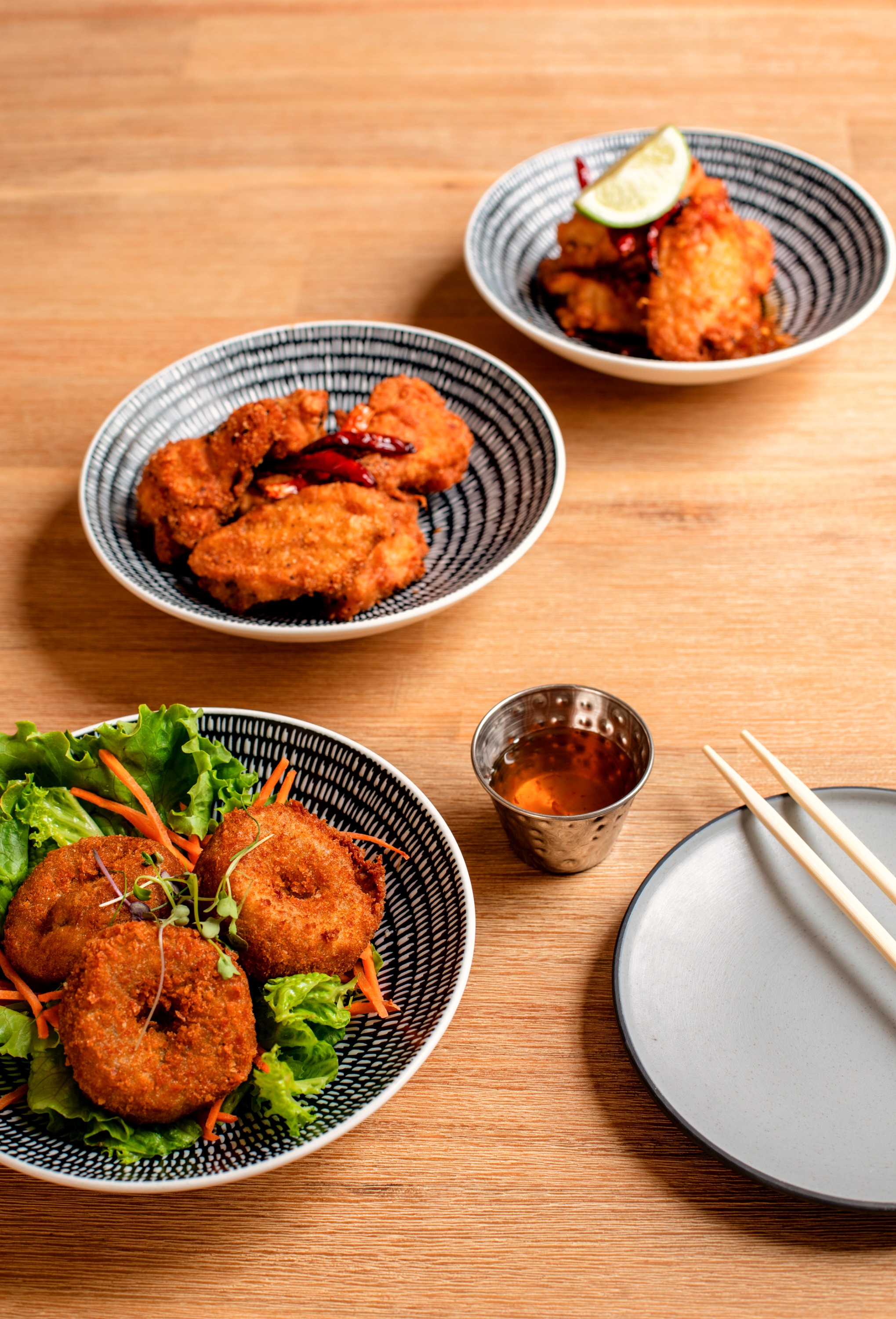Thai fried chicken and fish cakes in striped bowls with dipping sauce on a wooden table