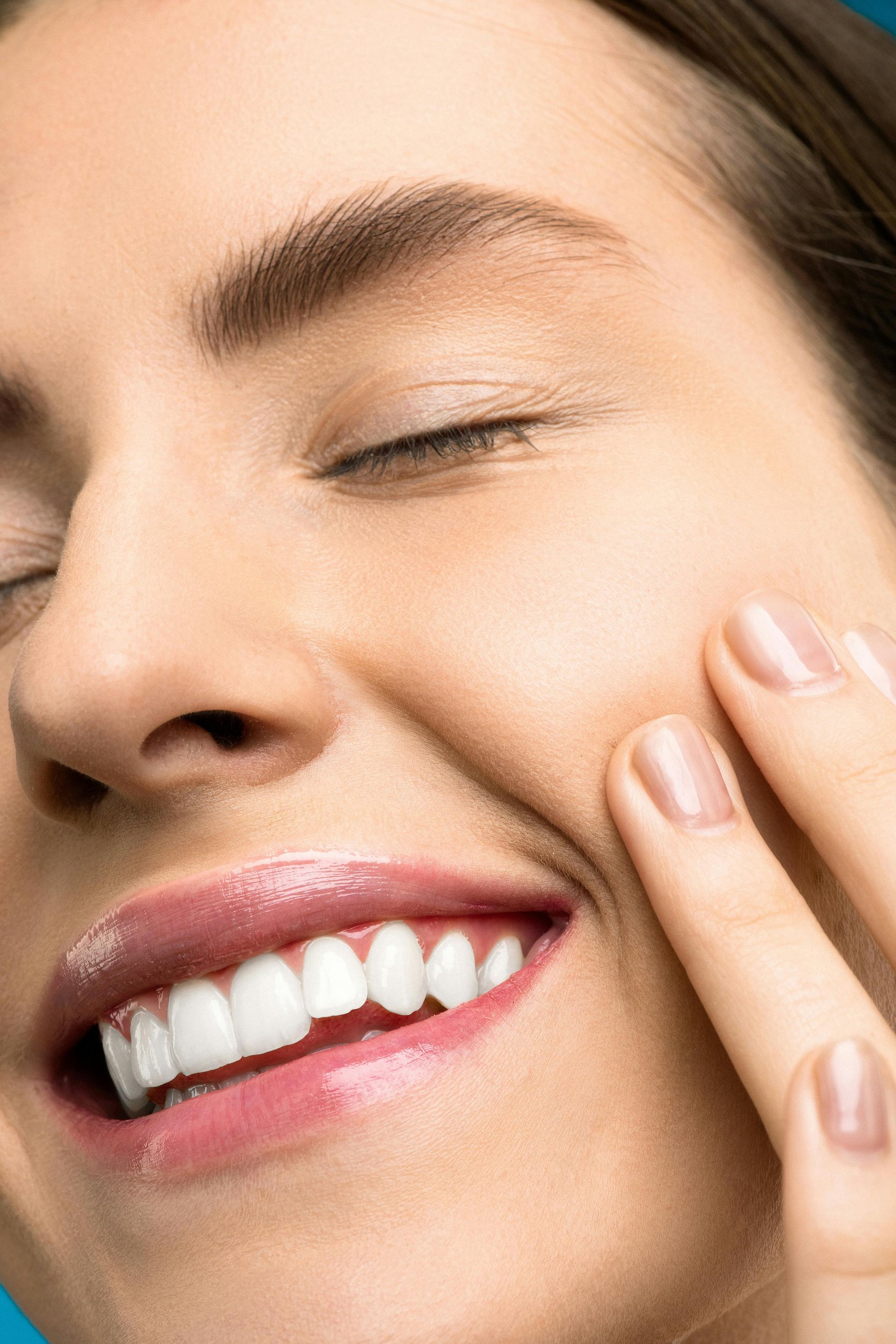 Smiling woman touching her cheek, teal background