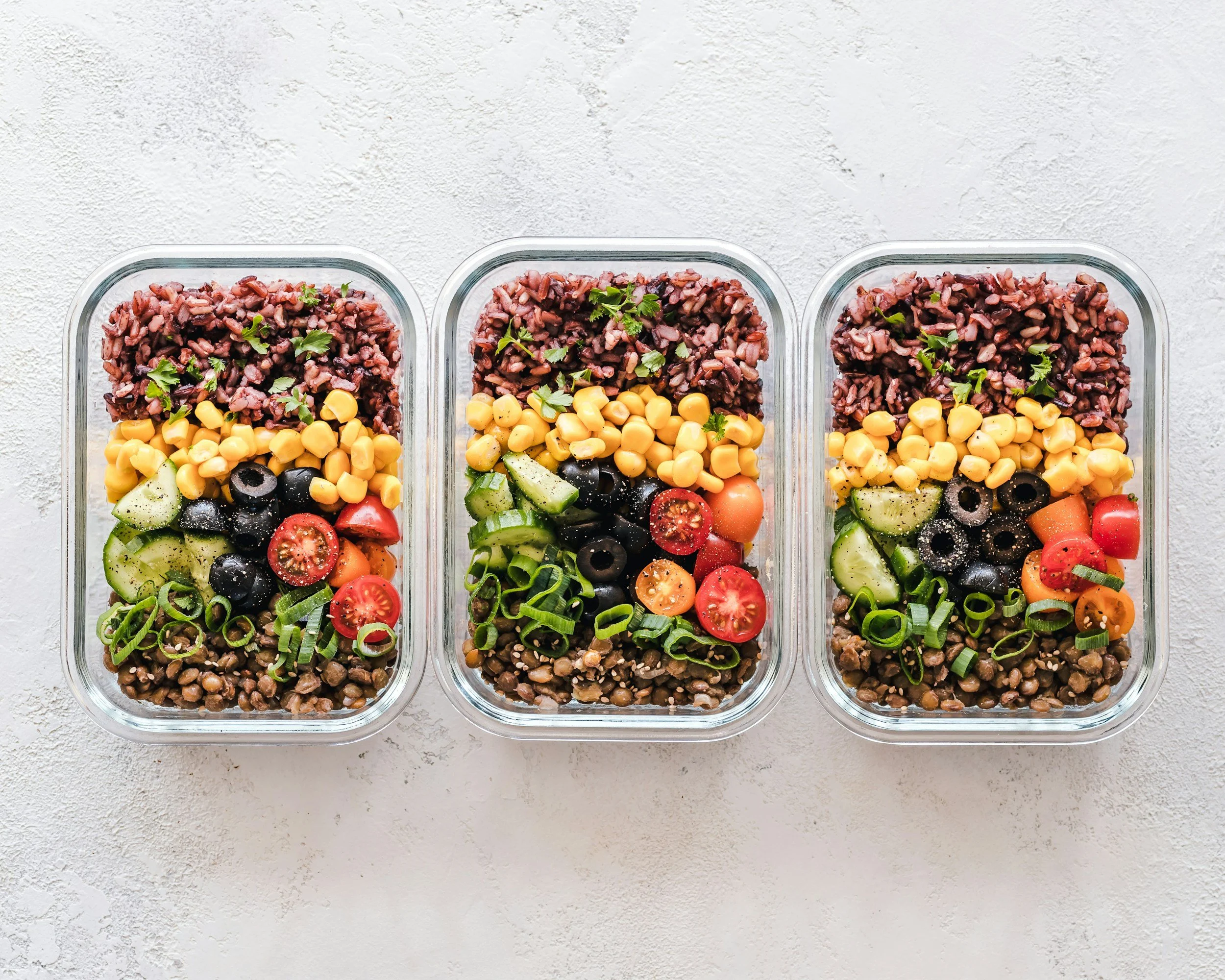 Three glass meal-prep containers filled with colorful layered vegetables, grains and legumes
