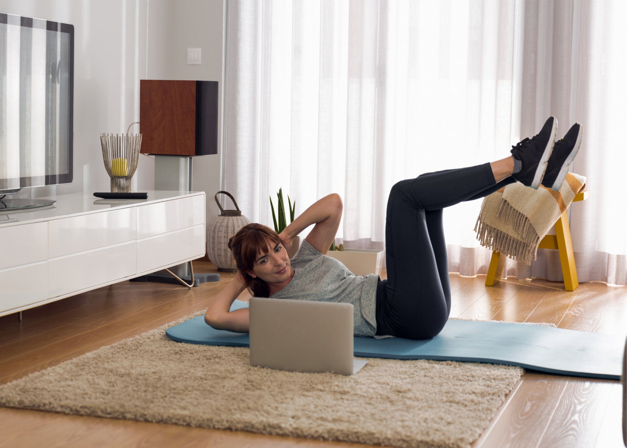 Woman doing crunches on a yoga mat at home with a laptop open in front of her
