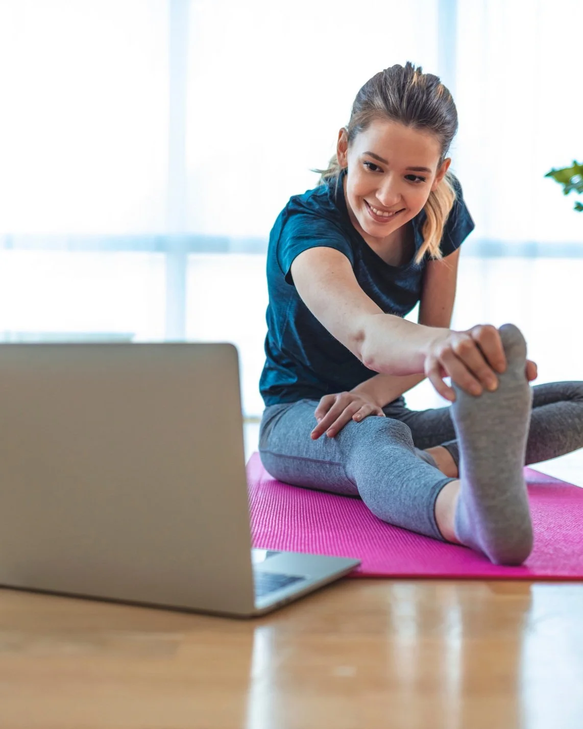 Young woman smiling while stretching on a pink yoga mat during a virtual workout