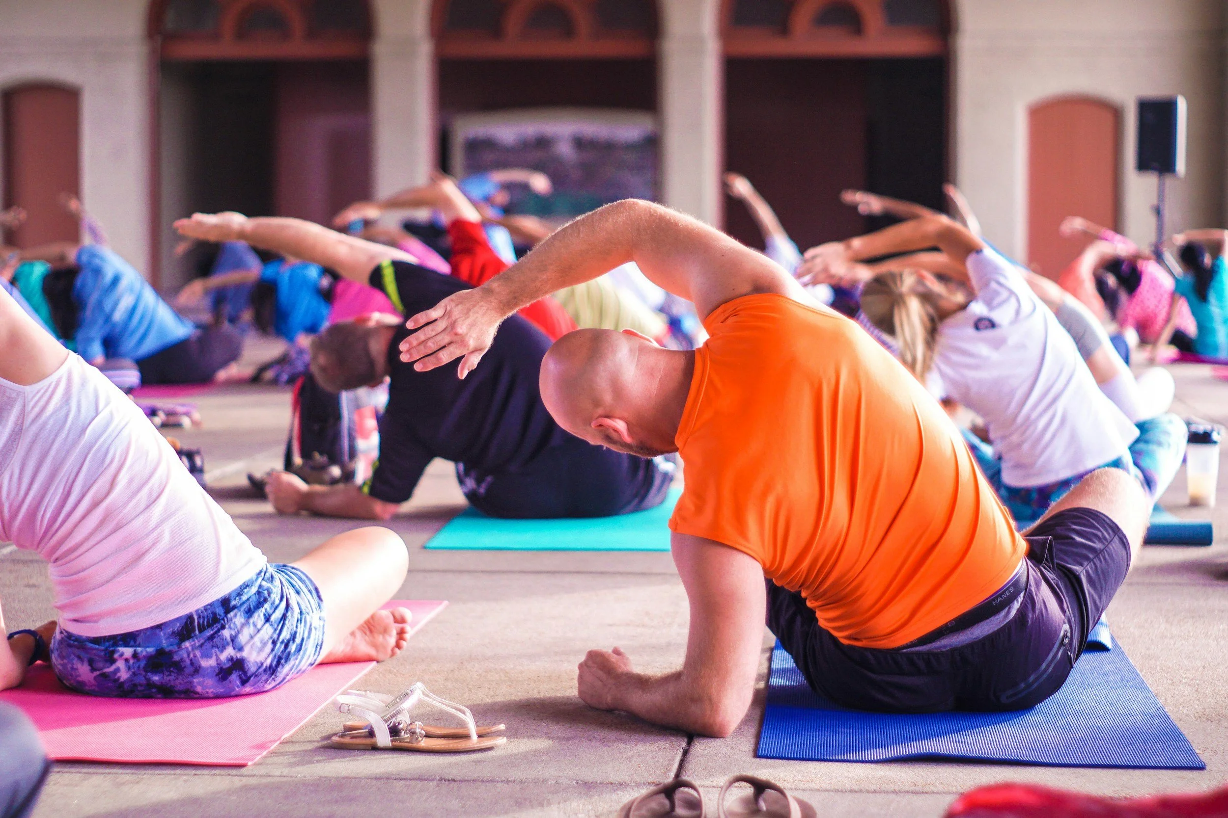 Large group yoga class stretching on colorful mats in an open hall