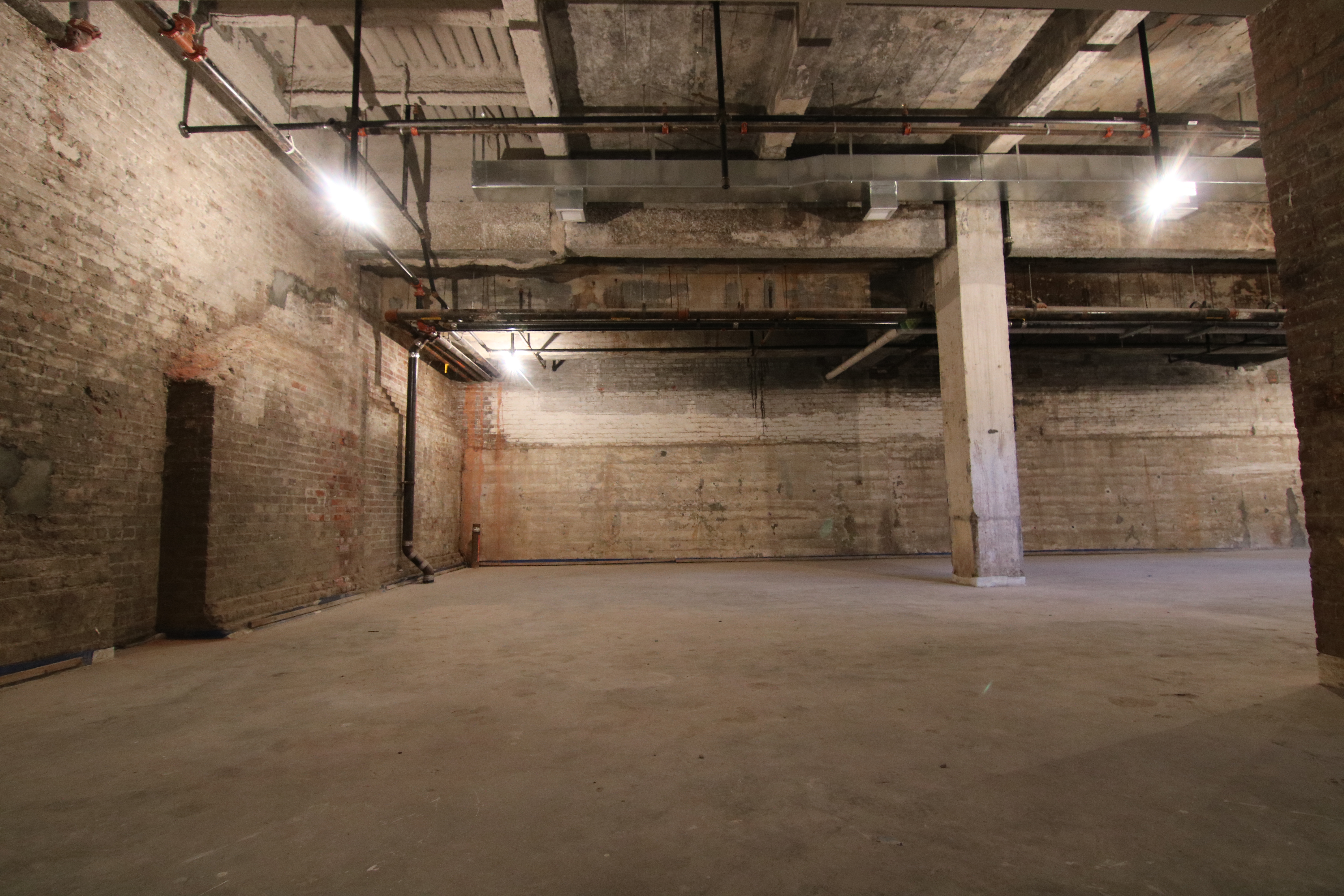 Dark raw basement studio with exposed brick walls, concrete ceiling and industrial piping