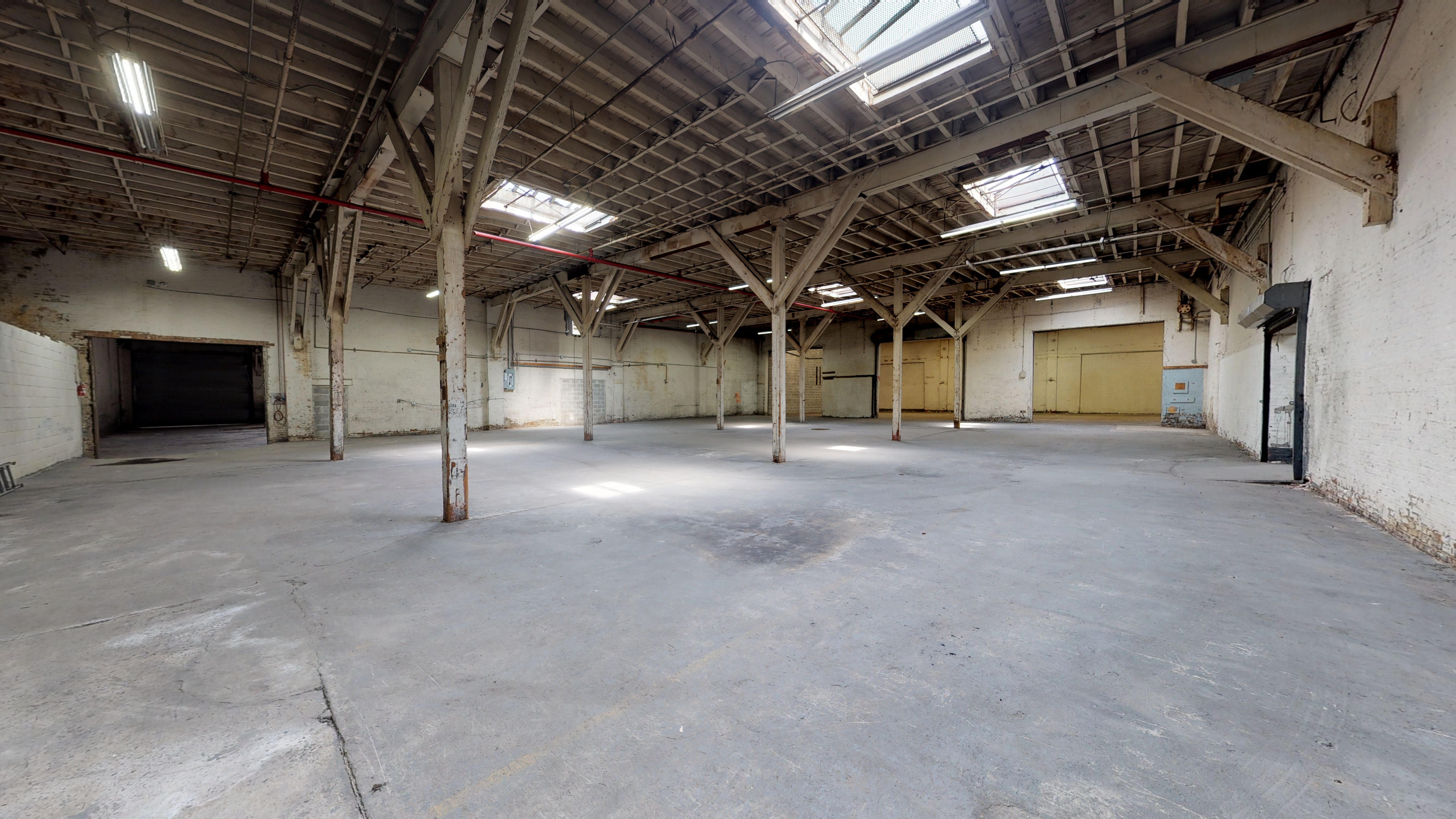 Vast raw warehouse interior with concrete floor, wooden truss ceiling and skylights