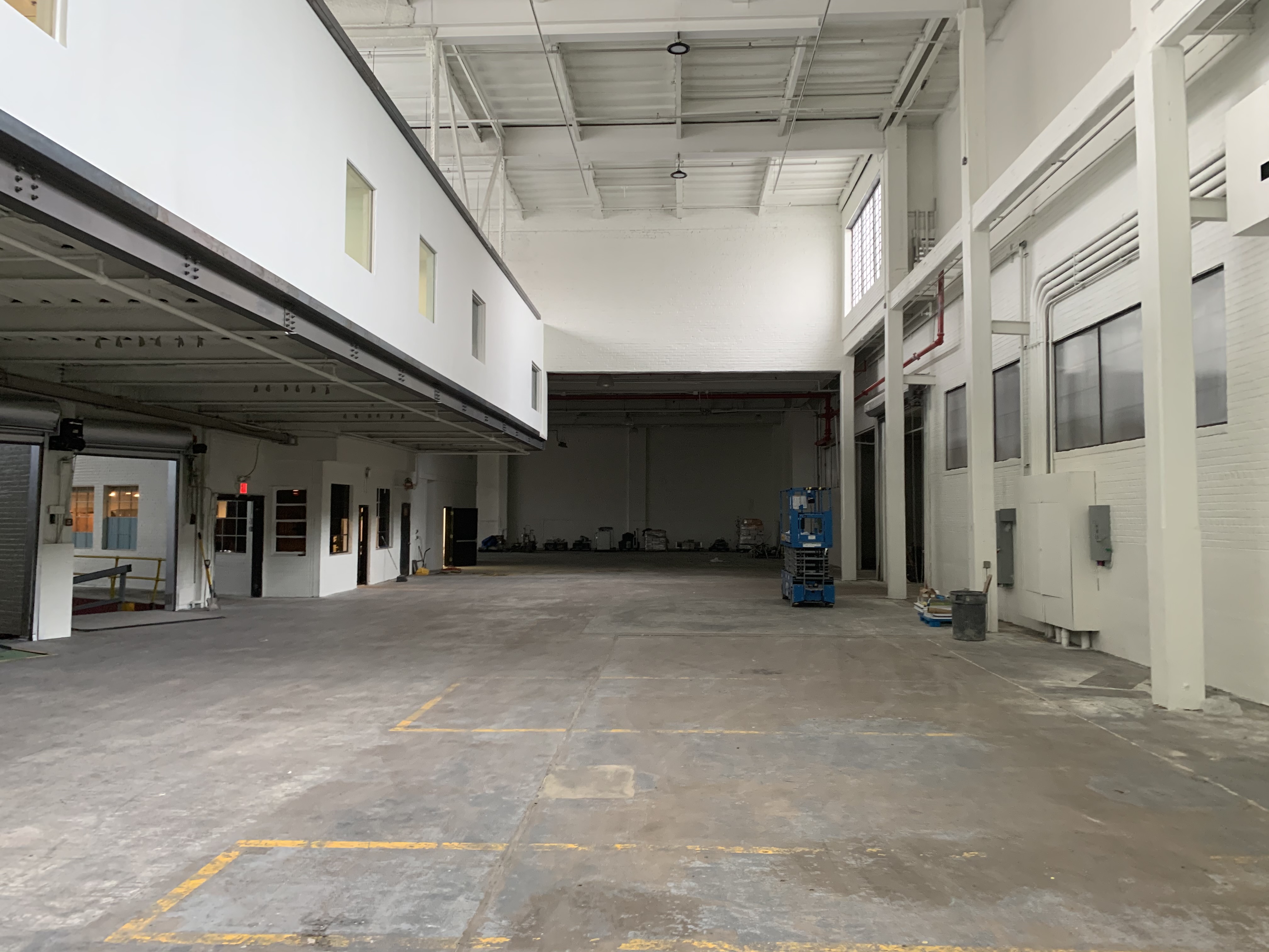 Large white-walled industrial studio with high ceilings, concrete floors and construction equipment