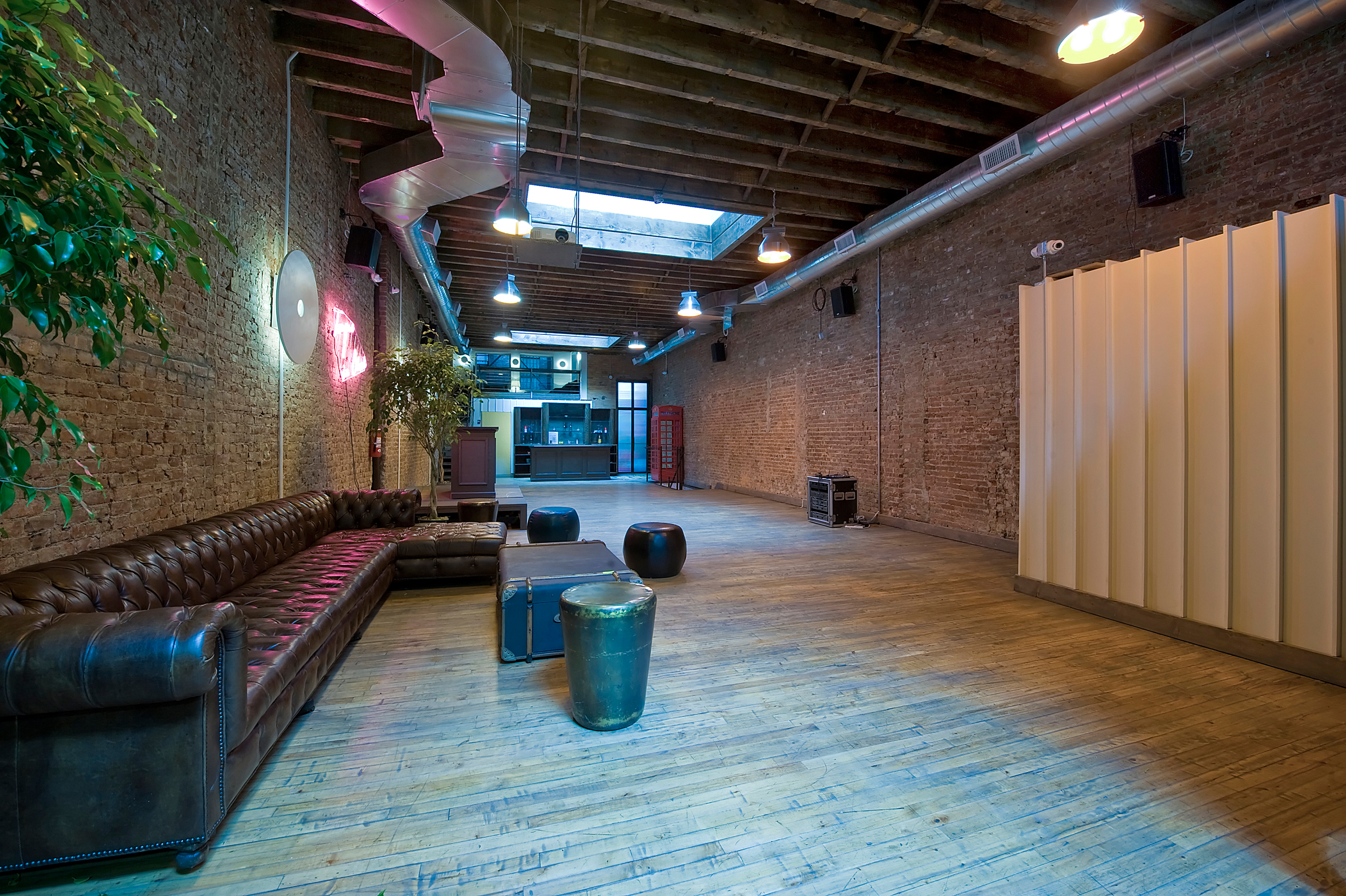 Furnished industrial loft event space with leather Chesterfield sofas, exposed brick, wooden floors and a bar area