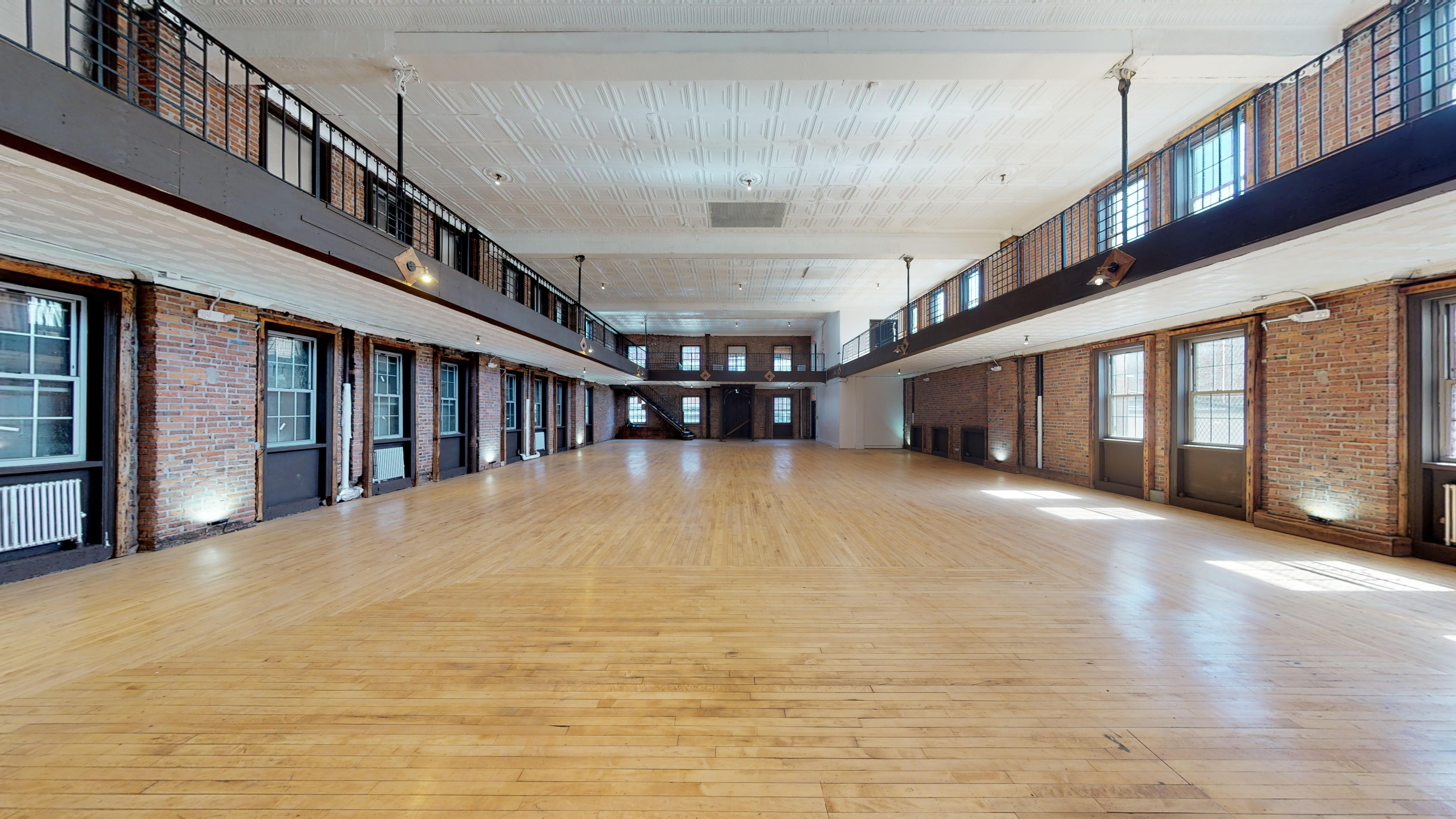 Large open loft studio with exposed brick walls, mezzanine balconies and hardwood floors