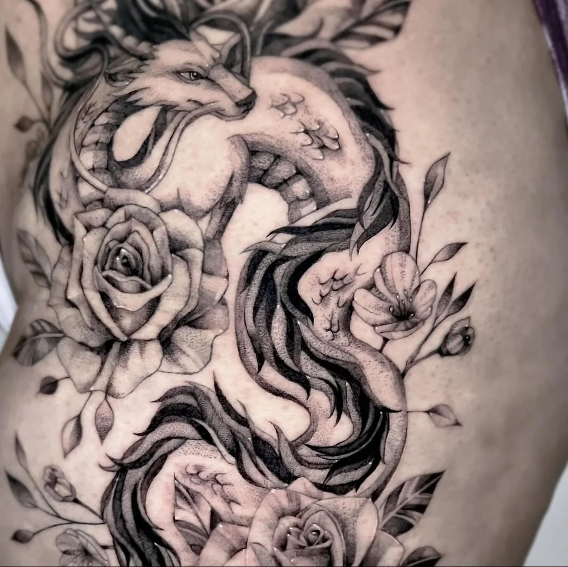 Large black-and-grey fine-line tattoo of a fox with flowing tails surrounded by roses and flowers, on a torso and rib area