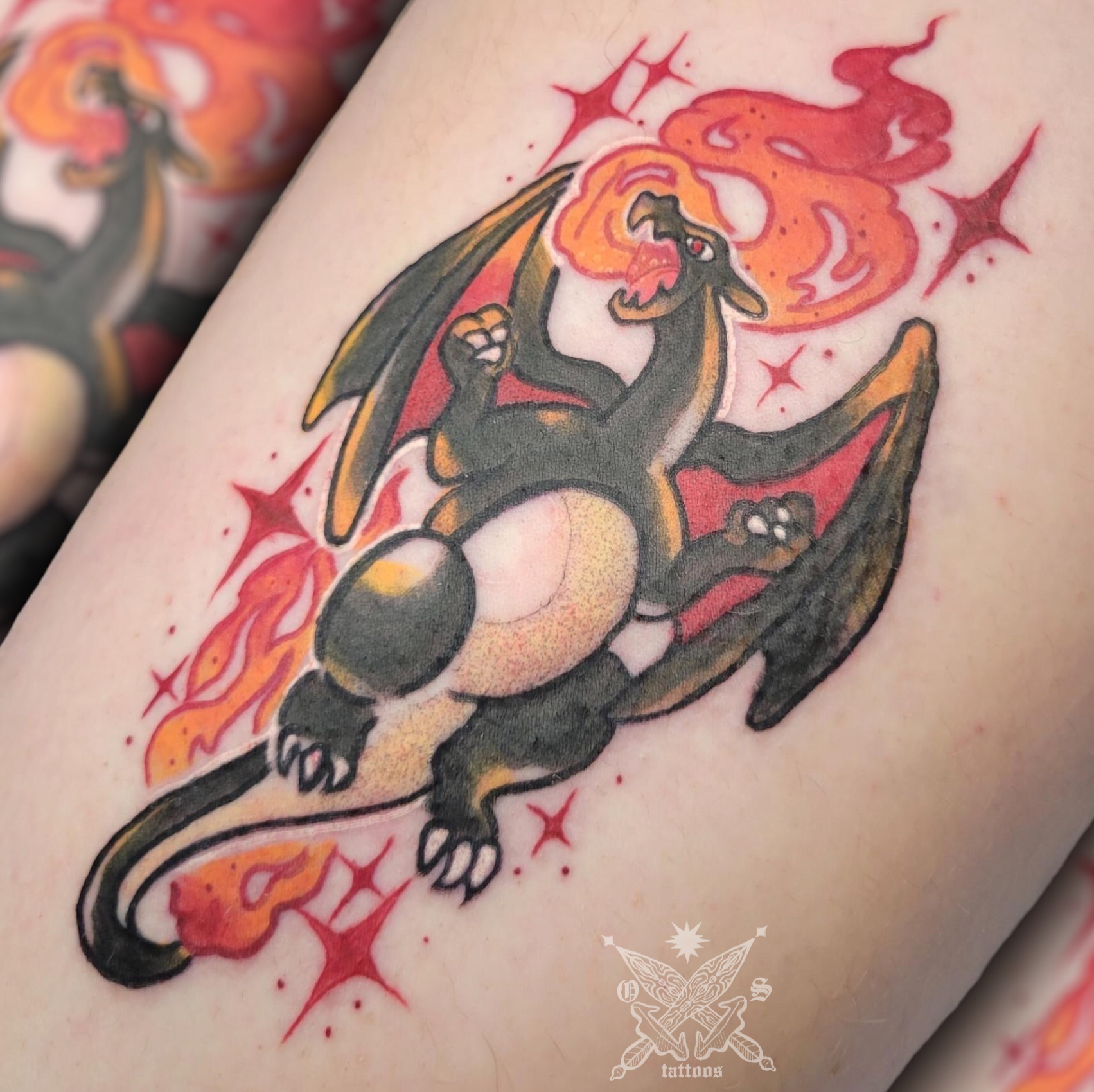Color tattoo of a dark Charizard surrounded by orange flames and red sparkles, on an arm