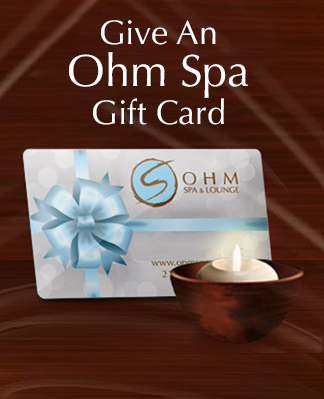Ohm Spa gift card with a blue bow and a lit candle on dark wood