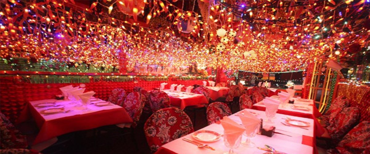 Wide-angle interior of Panna II: red tables, patterned chairs and a ceiling covered edge to edge in colored Christmas lights