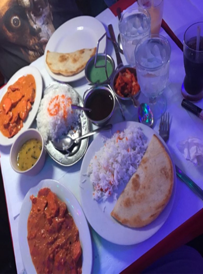 Curry, rice, naan and chutneys on a table under blue light