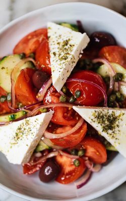Overhead shot of a Greek salad with feta, tomatoes, cucumbers, olives and capers on a white plate