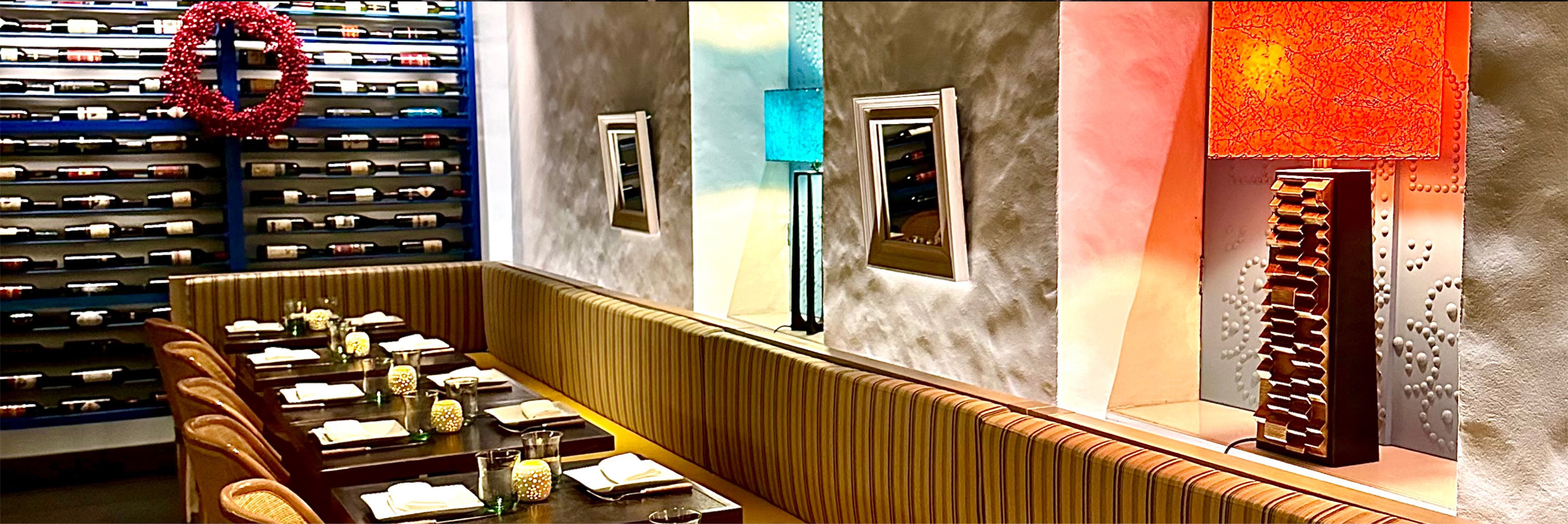 Pylos Restaurant interior: wine rack wall, striped banquette seating, set dining tables and colorful lamps