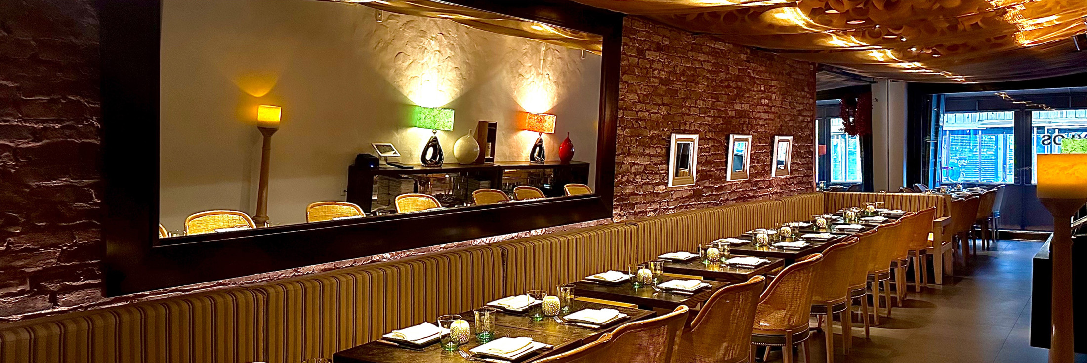 Pylos dining room with exposed brick walls, a large mirror, striped banquette seating and set tables