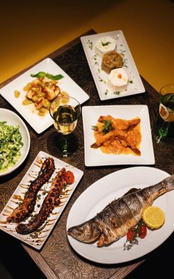 Overhead spread of Greek dinner dishes including whole fish, octopus, shrimp and meze plates