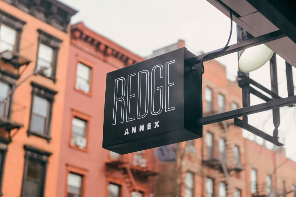 Black projecting street sign reading Redge Annex against a red-brick East Village building