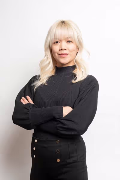 Redge Salons stylist Regina, blonde hair, wearing black, arms crossed, on a white studio background