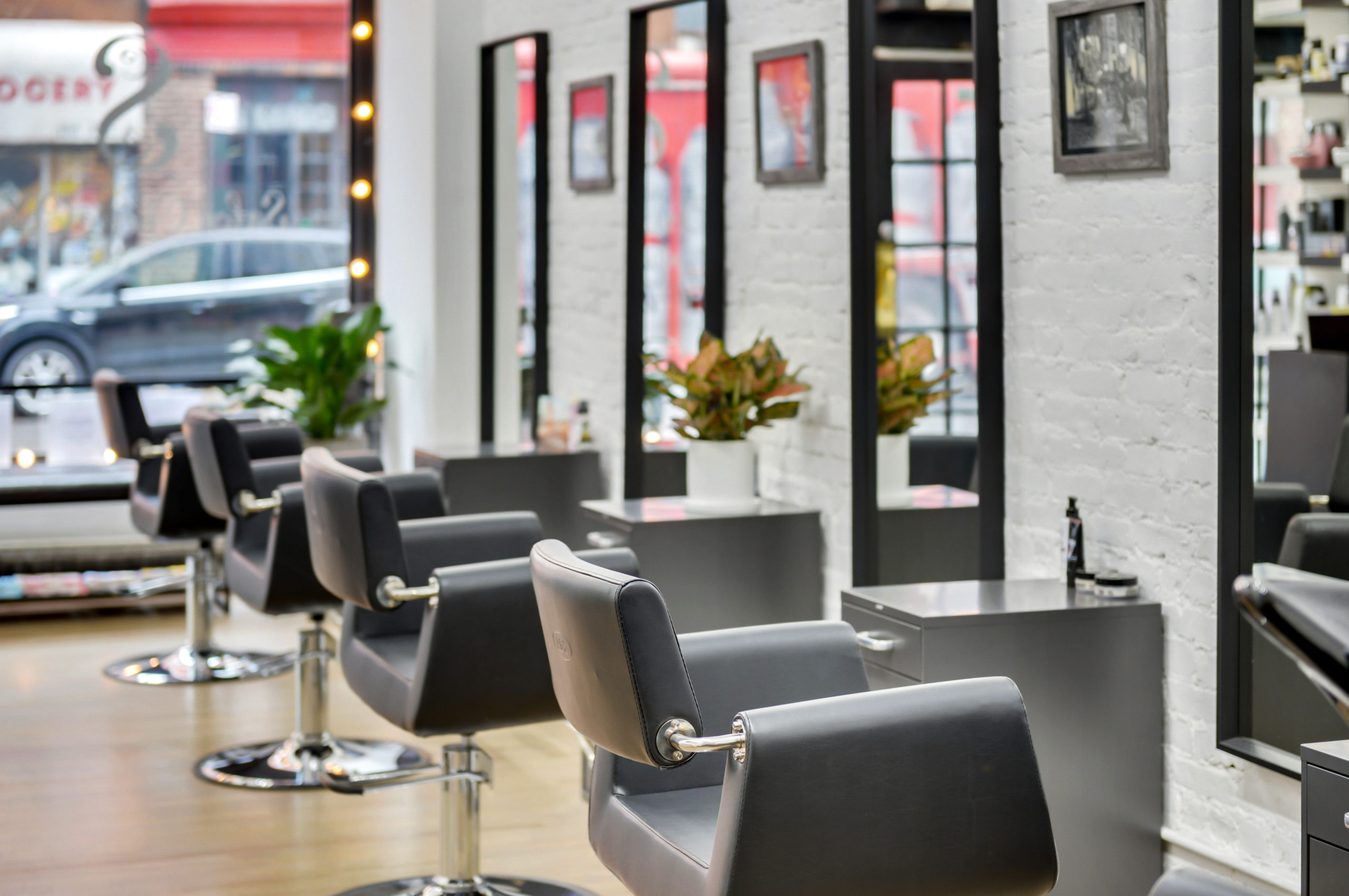 Interior of Salon Chérie Chéri — a row of grey styling chairs, bulb-lit mirrors and white brick walls