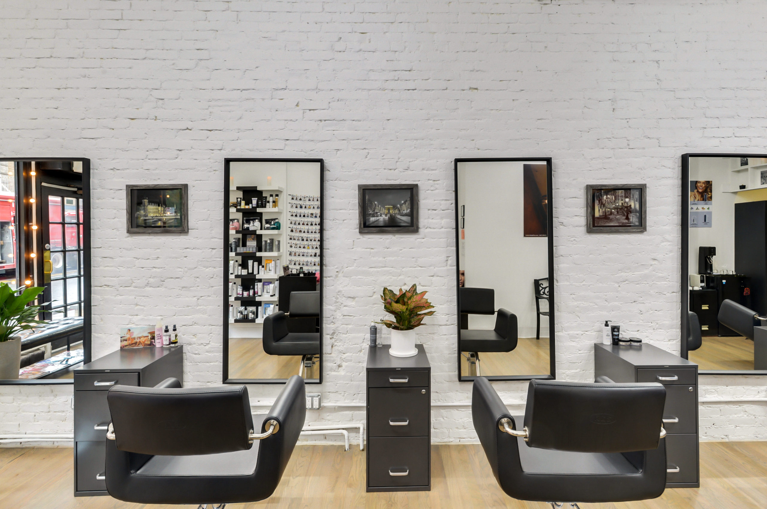 Salon interior — two styling chairs facing full-length mirrors against white brick, product shelves reflected