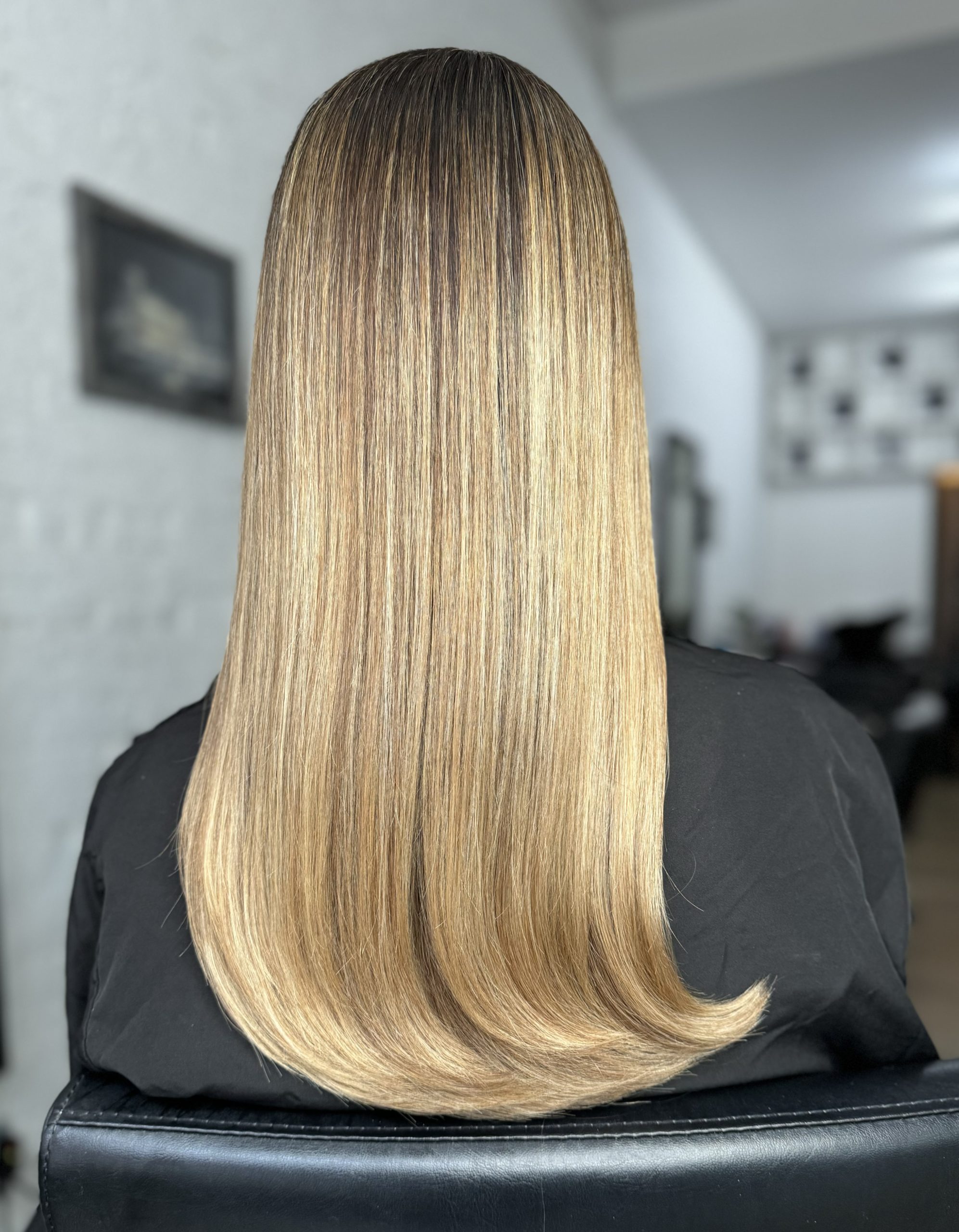 Back view of long straight golden-blonde balayage hair in a salon chair