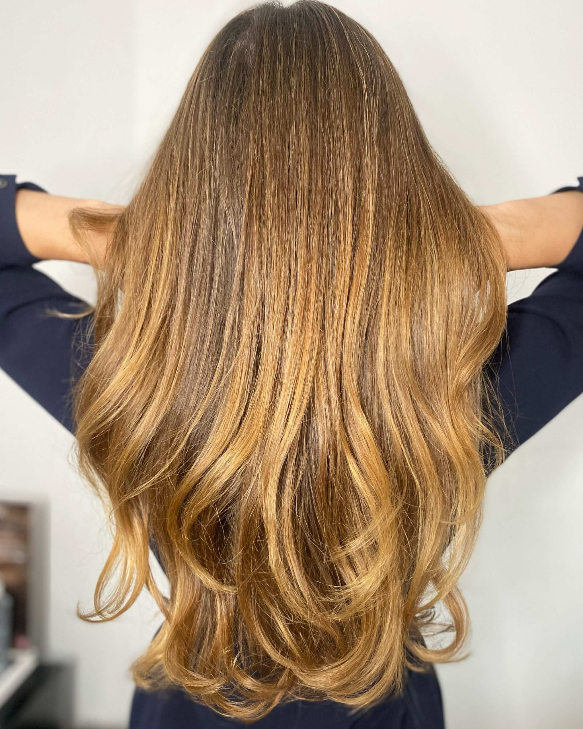 Back view of long golden-brown balayage hair with hands raised behind the head