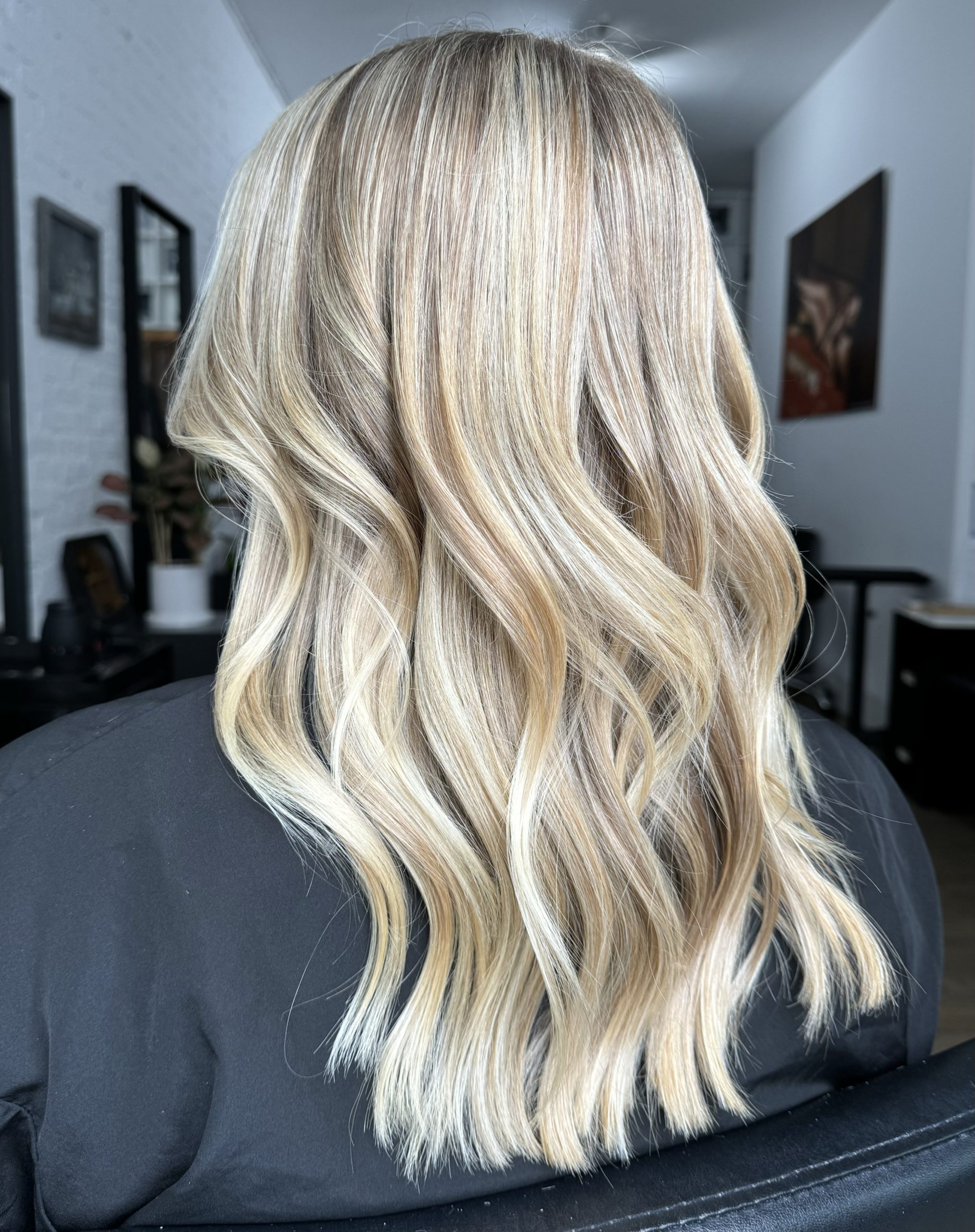 Back view of long wavy blonde highlighted hair inside the salon