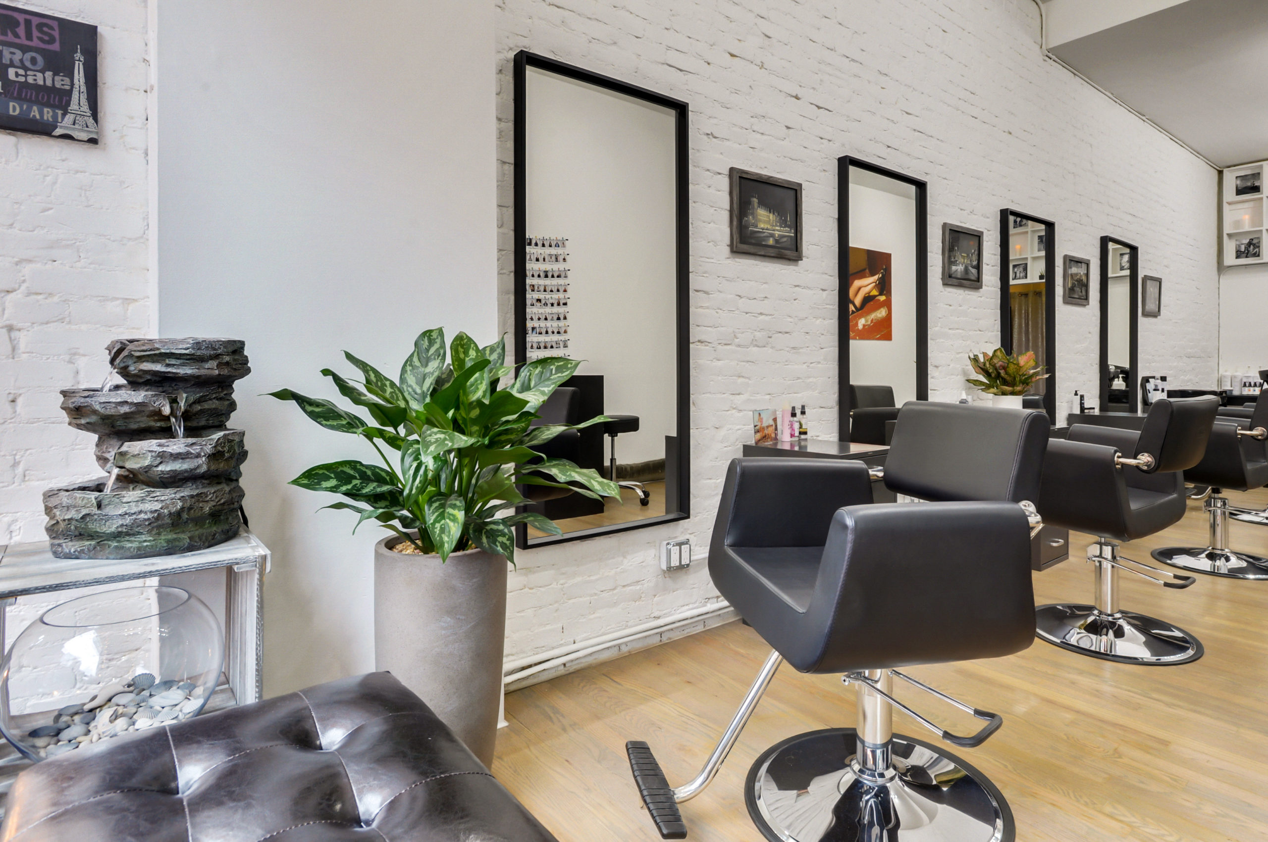 Salon interior — black styling chairs, mirrors, plants and a stone water fountain