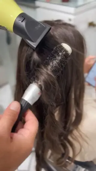 Stylist round-brush blow-drying dark wavy hair