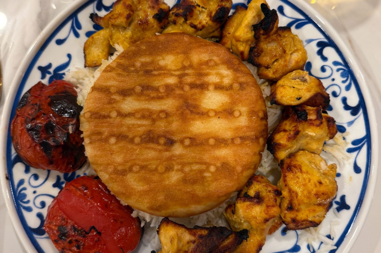 Saffron chicken kabob with tahdig rice, grilled tomato and taftoon bread on a blue-and-white Persian plate