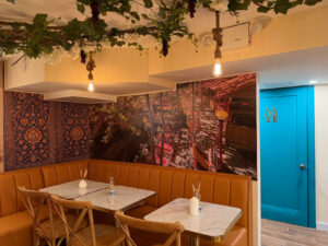 Booth seating under the floral ceiling with Persian rug wall art and a teal door accent