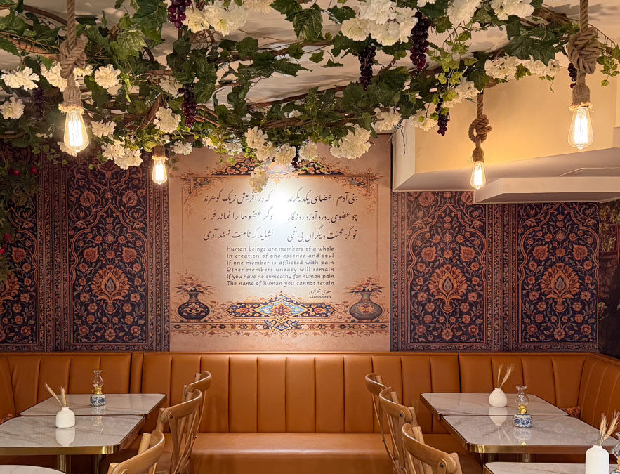 Taftoon dining room at night — leather banquettes, Persian-motif wallpaper, a Saadi Shirazi poem mural and a floral ceiling strung with Edison bulbs