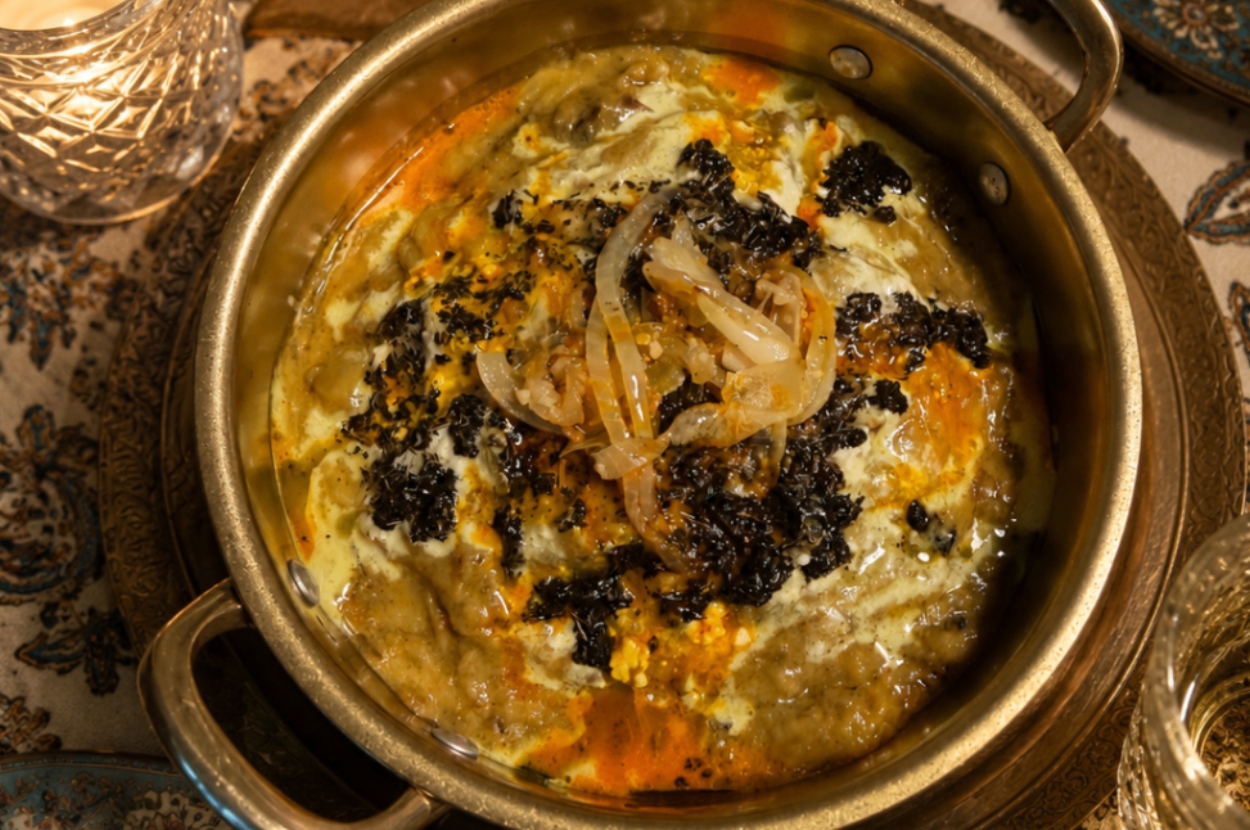 Ash Reshteh — Persian herb and noodle soup in a brass pot topped with kashk, fried onion and dried mint