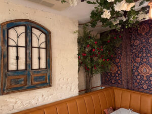Distressed blue arched window with climbing red roses above a leather booth and Persian rug accent wall