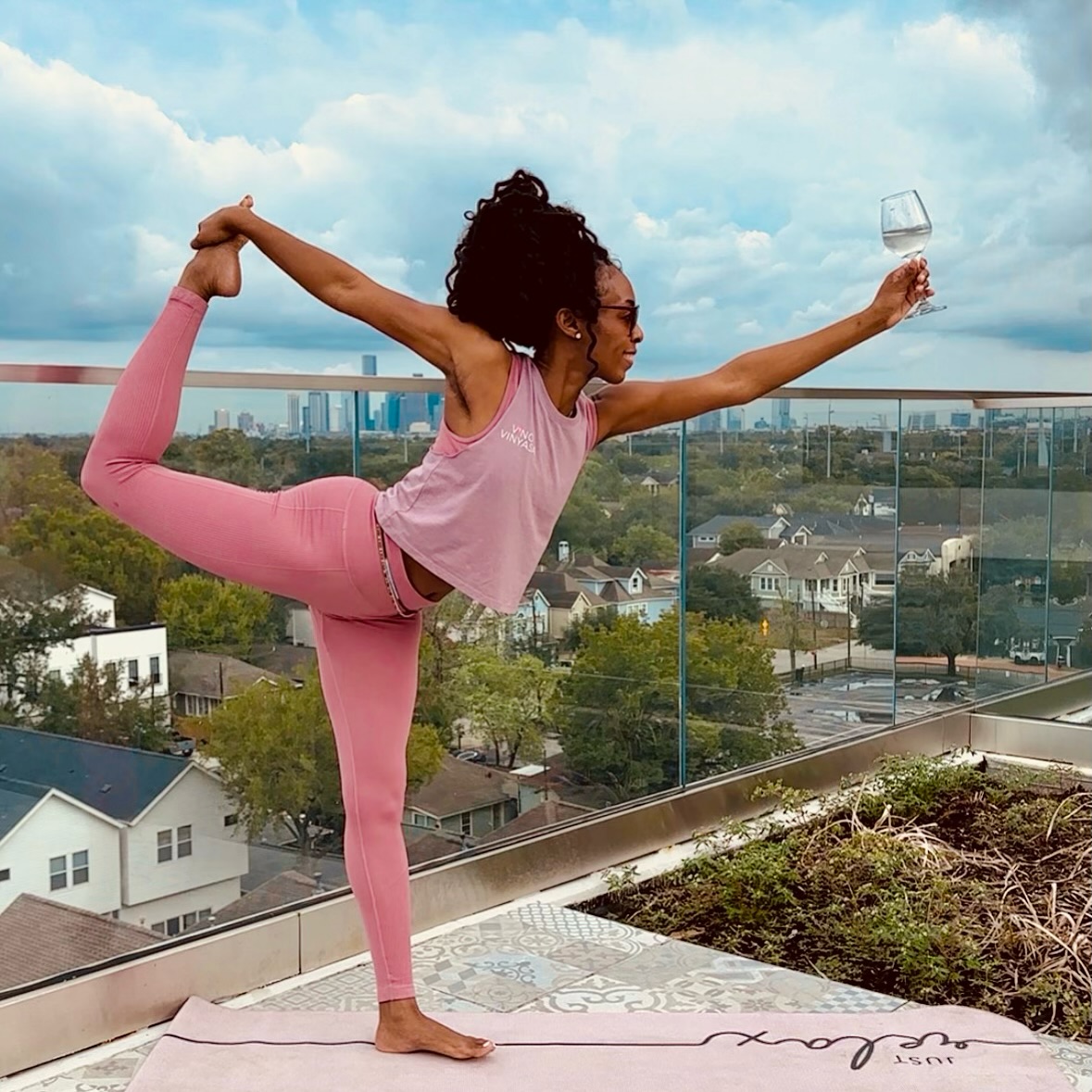 Woman in pink Vino Vinyasa tank doing dancer pose on a rooftop with city skyline