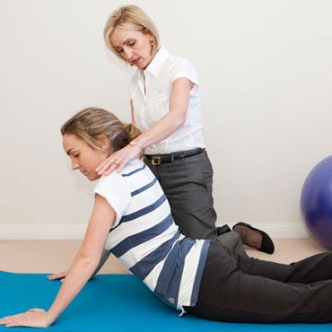 Therapist assisting a patient with a back stretch on a mat