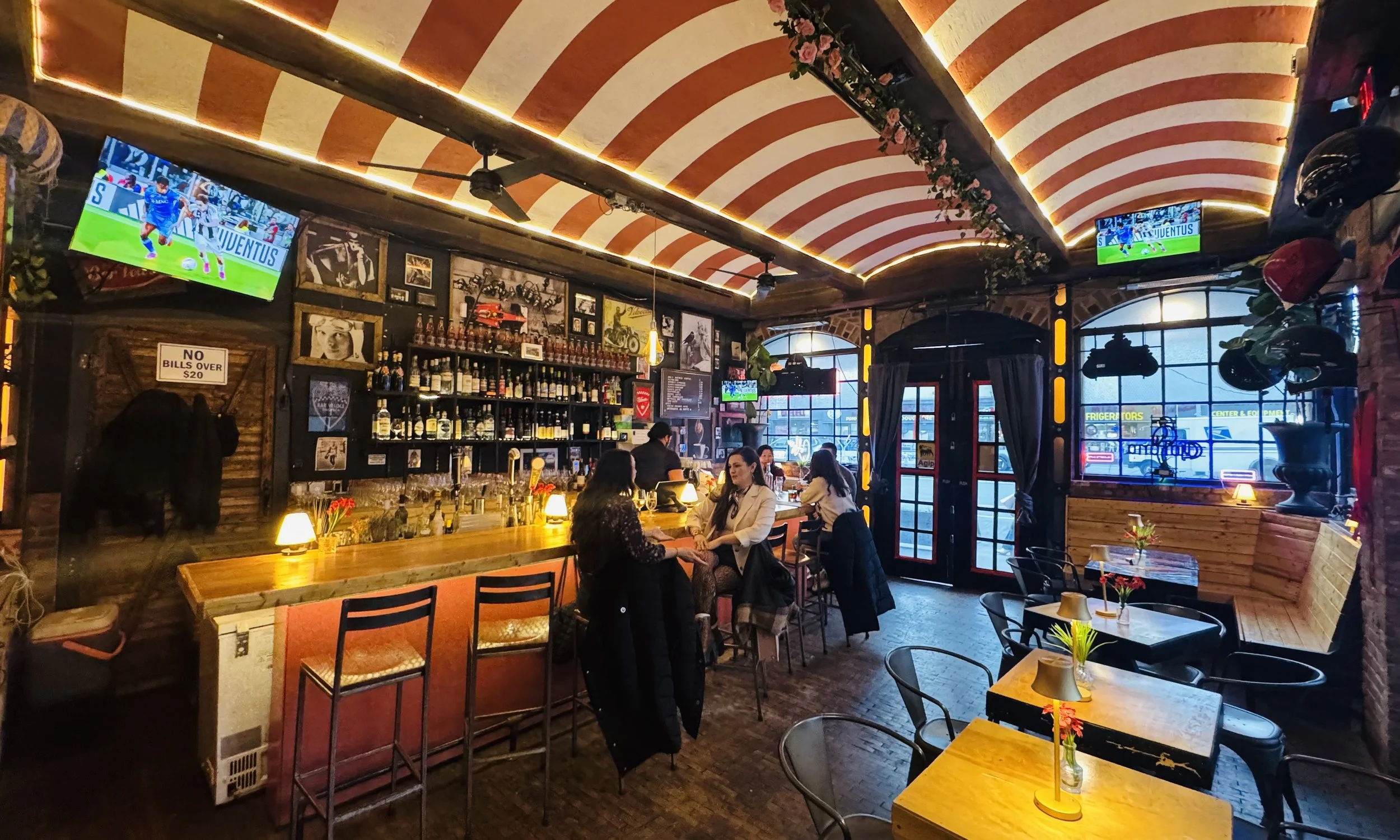 Bar Veloce Nolita interior — red and white striped arched ceiling, patrons at the bar, soccer on the screens