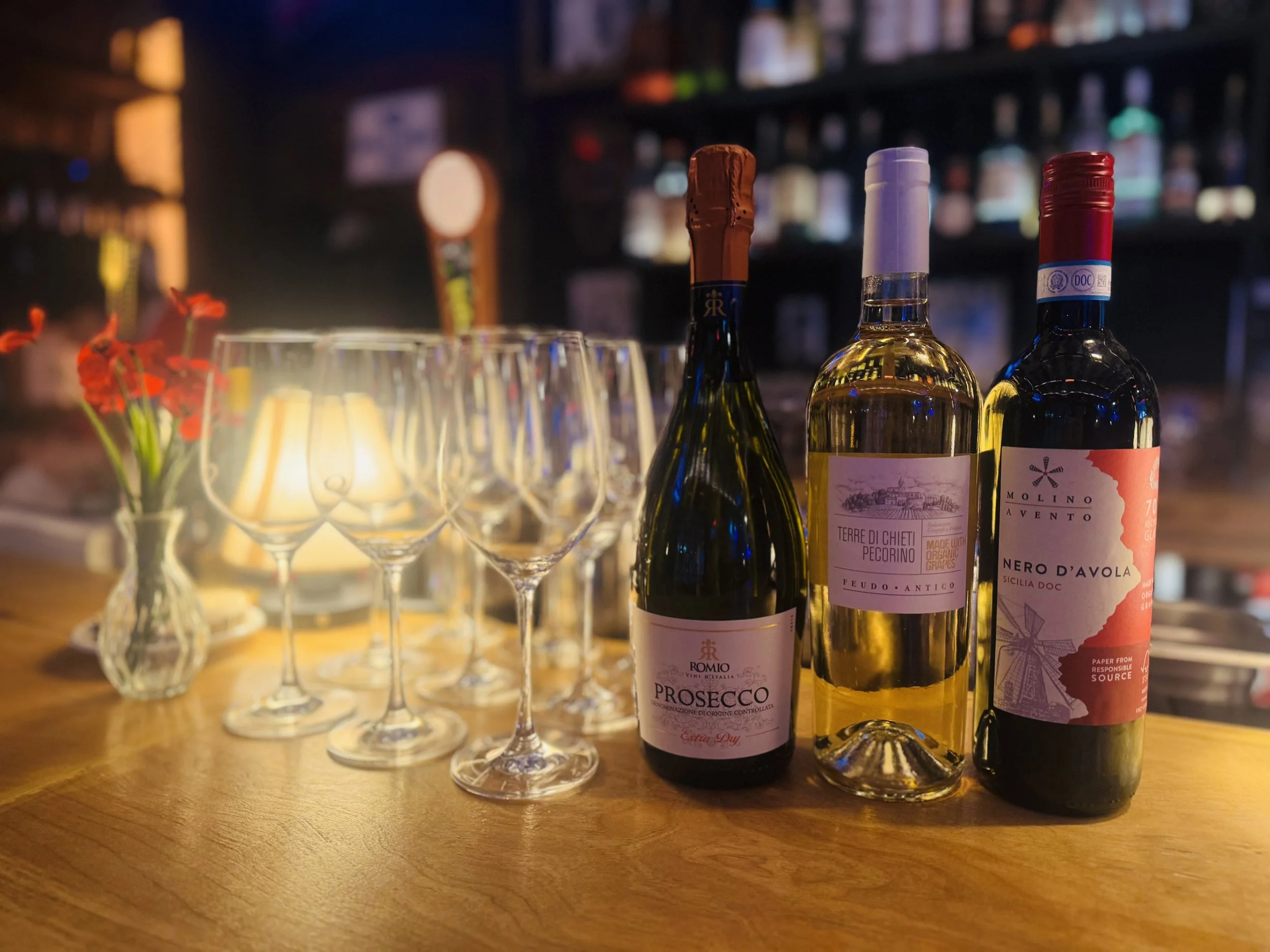 Three Italian wine bottles and empty glasses on the bar counter beside a candle