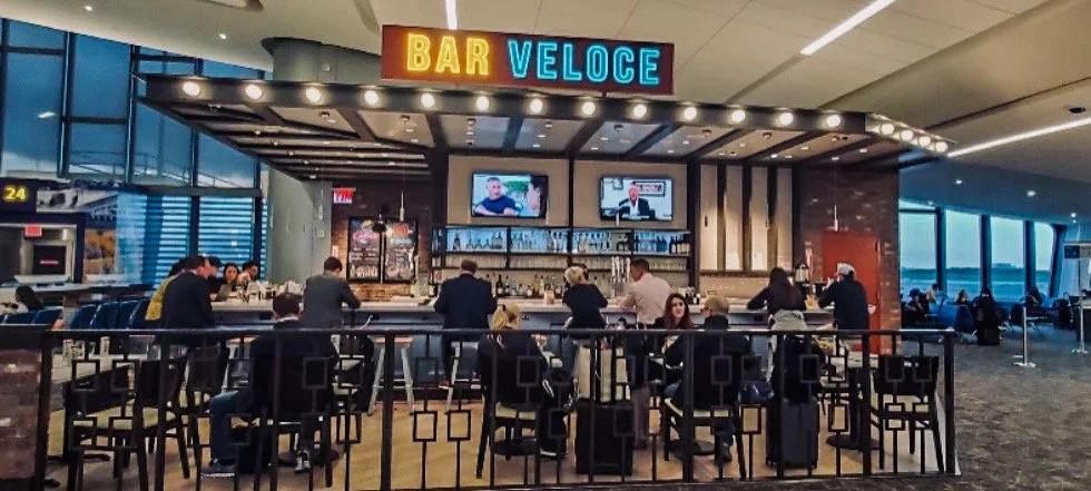 Bar Veloce at LaGuardia Airport Terminal B — illuminated Bar Veloce sign above a circular bar kiosk with seated guests
