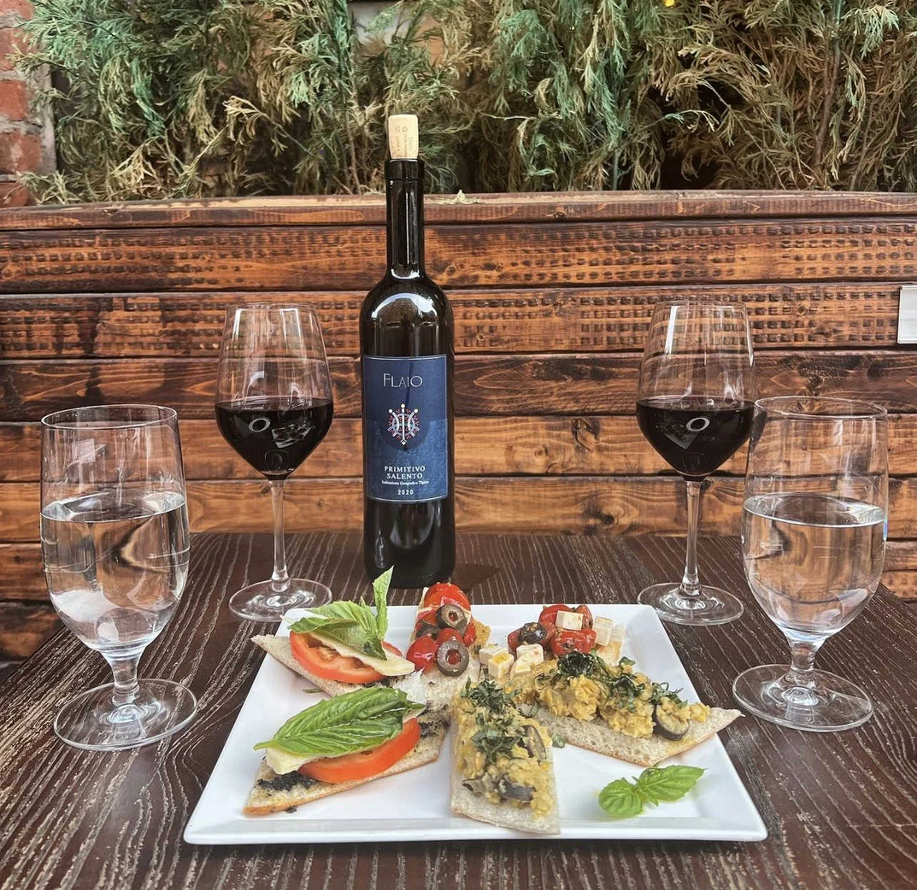 Bottle of Primitivo, two glasses of red wine and a plate of bruschette on an outdoor table