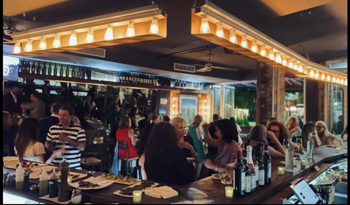 Busy East Village bar area filled with guests under Edison pendant lights