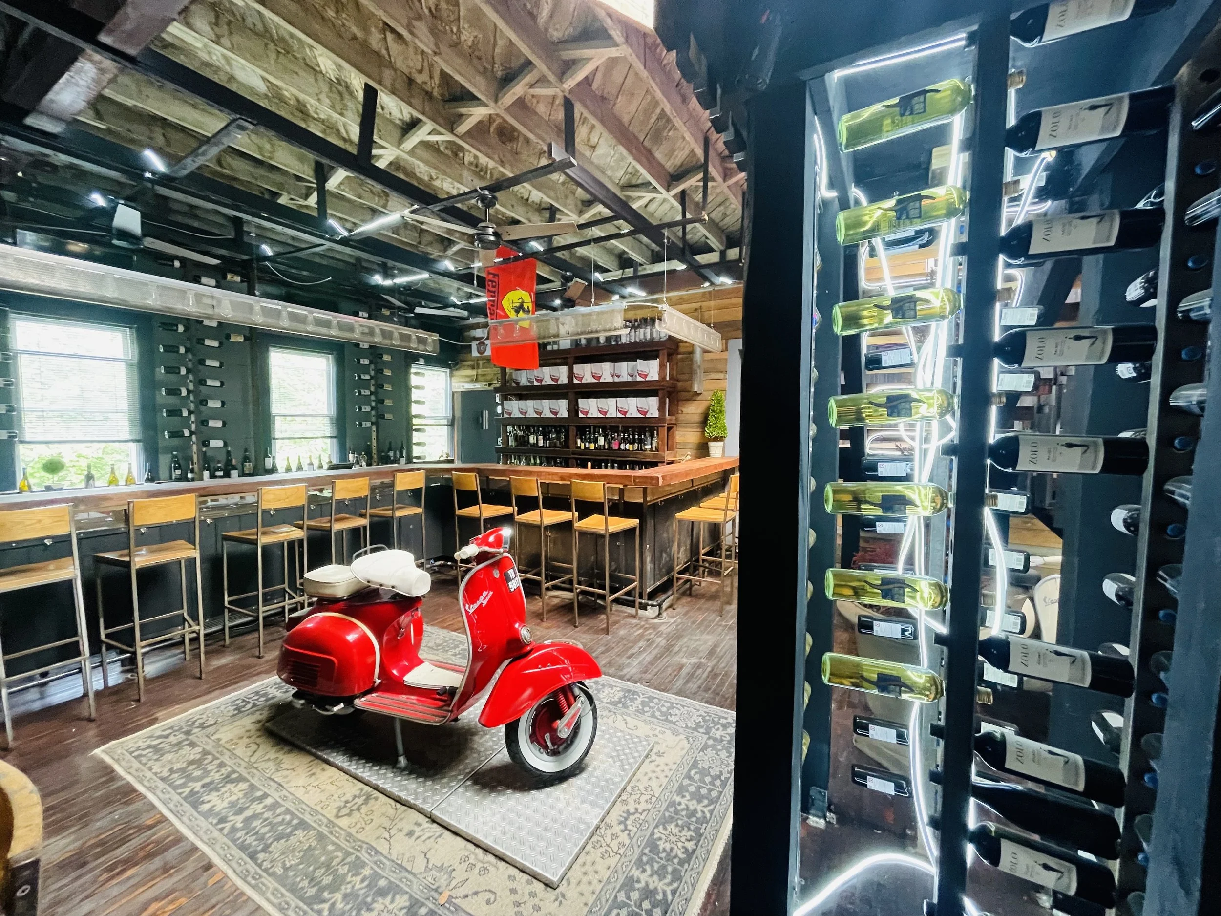 Bar Veloce Narrowsburg interior — a red Vespa on the floor in front of the bar and wine rack wall