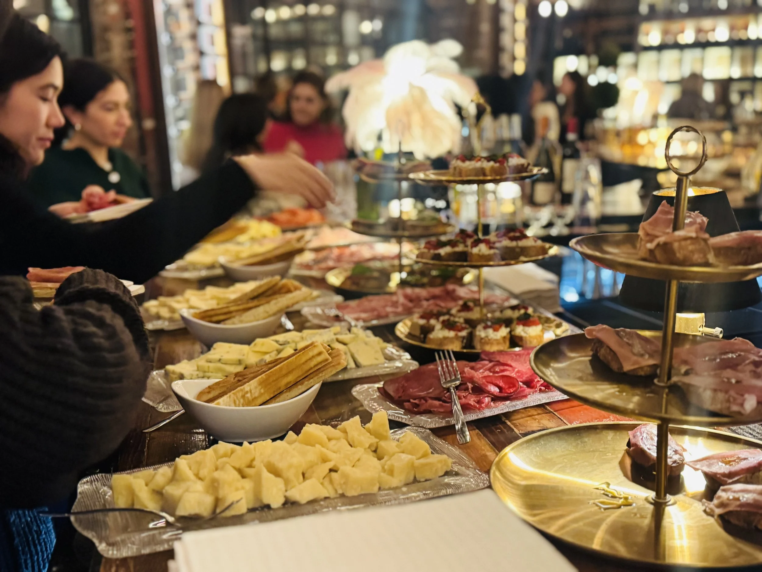 Guests serving themselves from an Italian aperitivo spread of cheese, charcuterie and bruschette