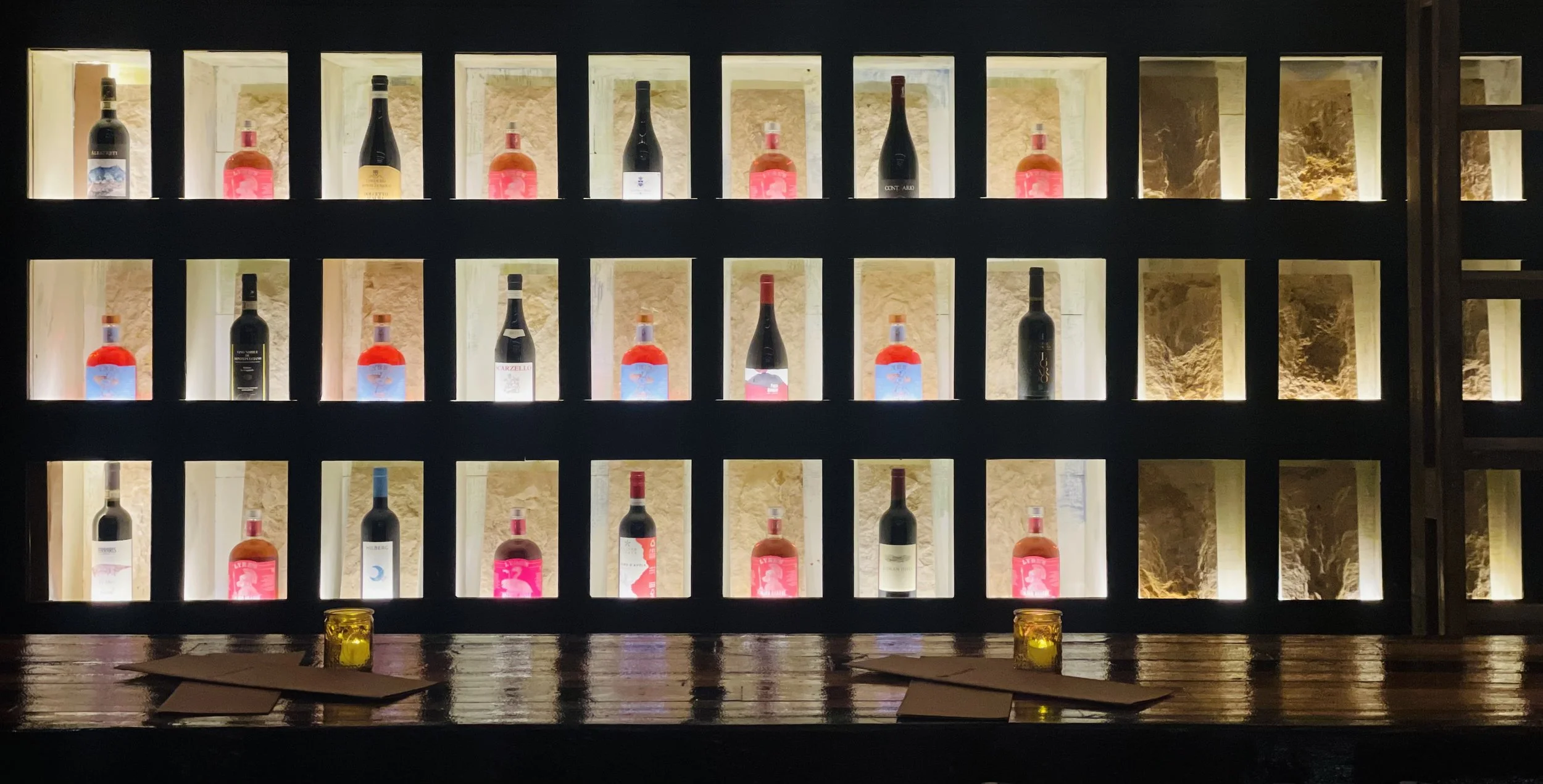 Backlit wine wall — a grid of illuminated niches each holding a single bottle