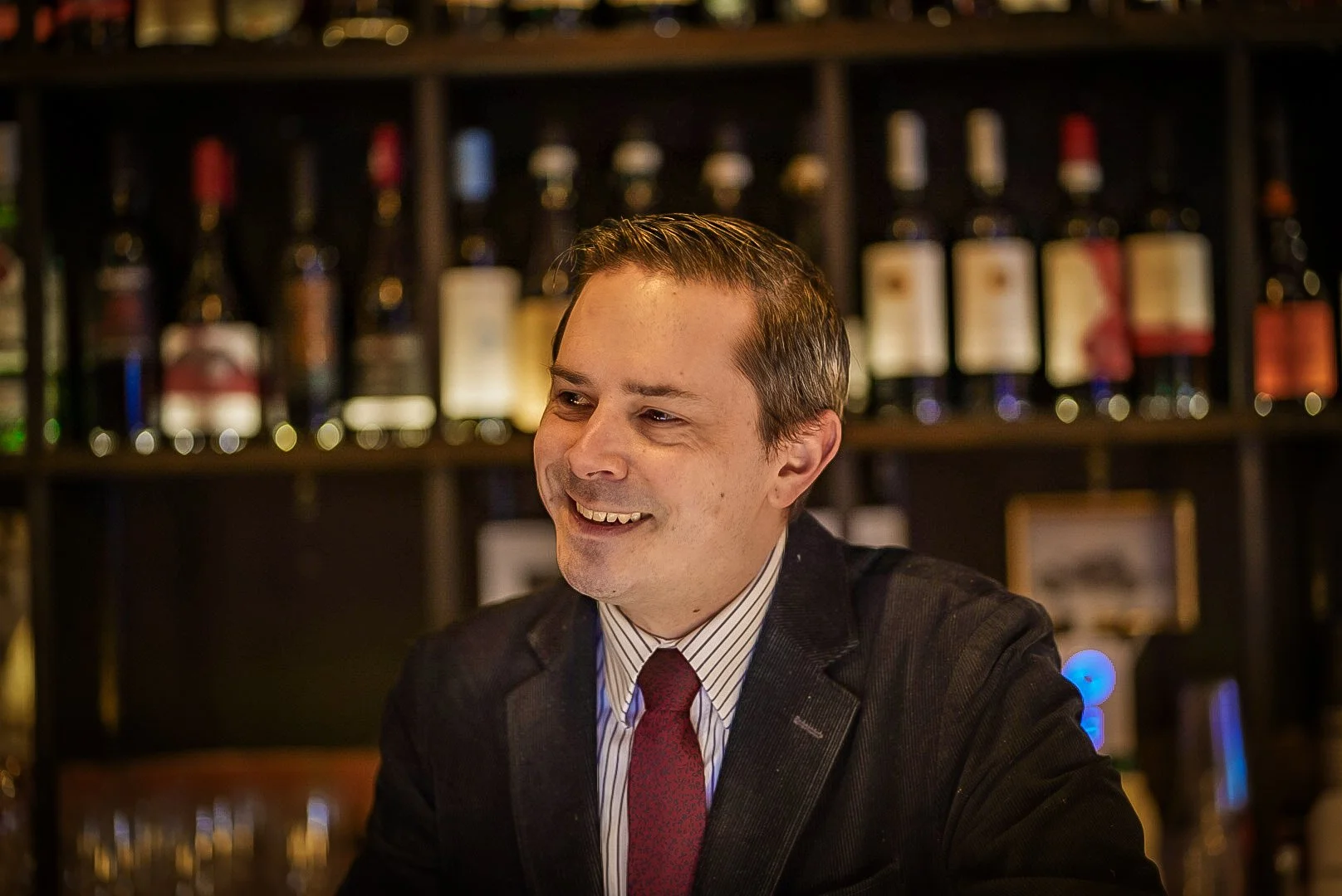 A host in a dark blazer and burgundy tie seated at the Bar Veloce bar