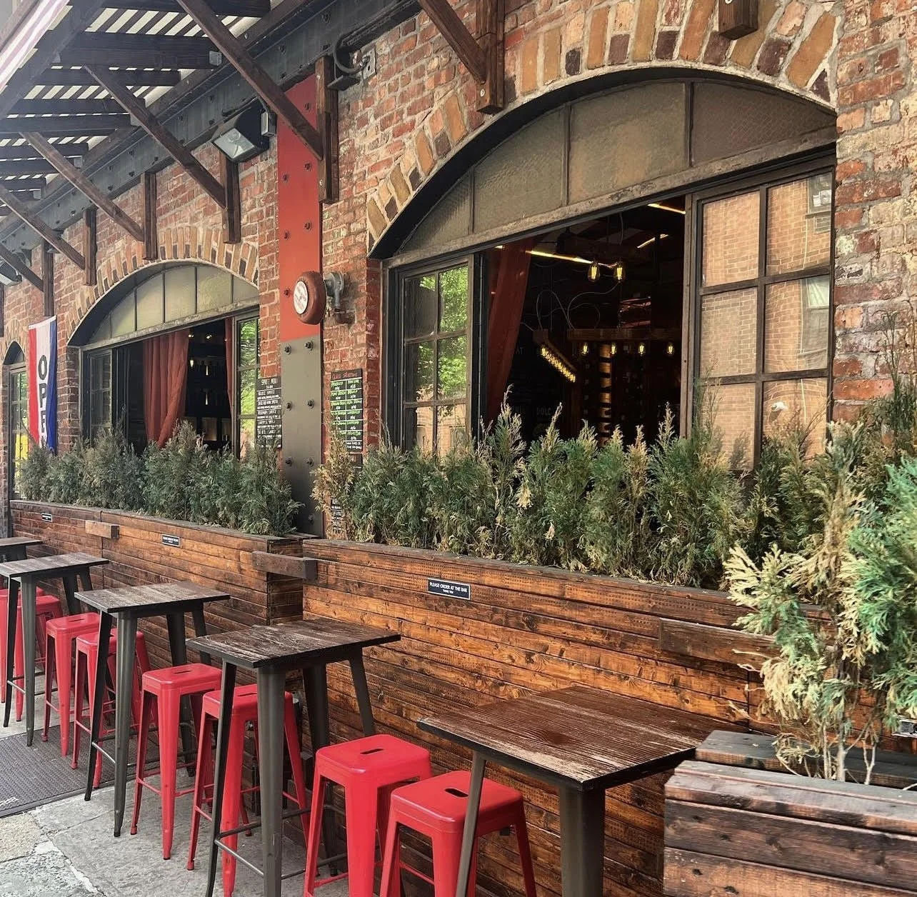 Bar Veloce sidewalk seating with red metal stools and hedge planters