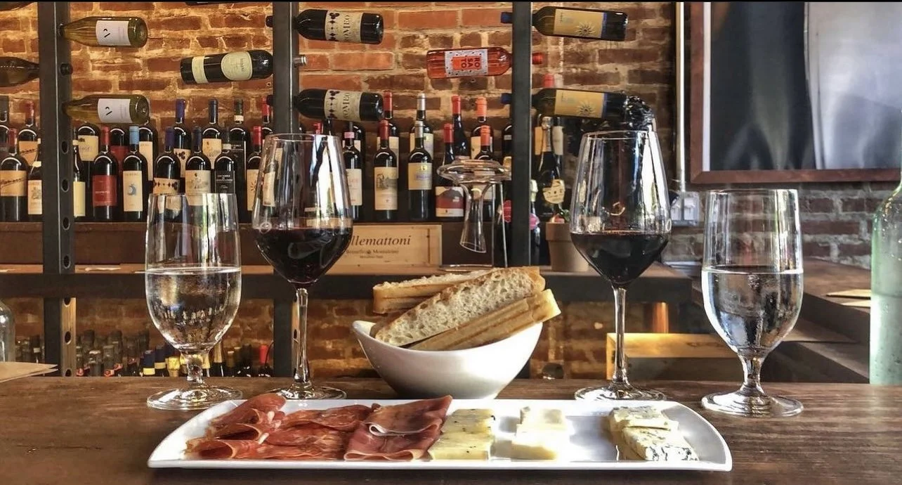 Charcuterie and cheese plate with two glasses of red wine in front of a brick wine wall
