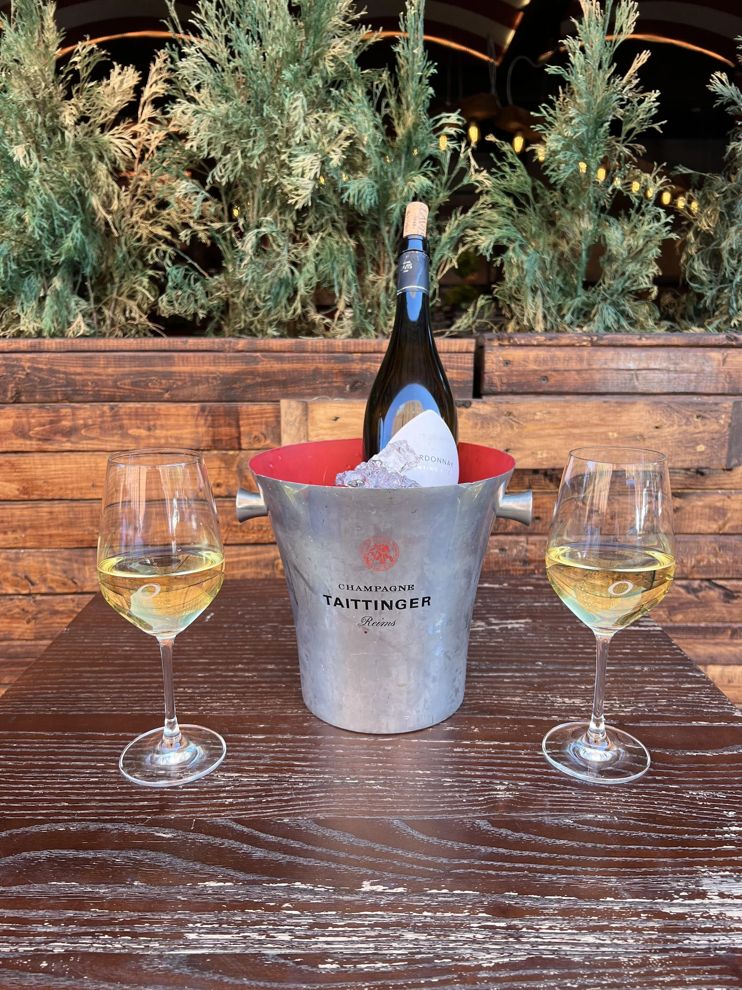 Champagne bucket with a bottle and two glasses of white wine on a wooden outdoor table