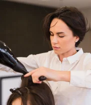 Hairstylist blow-drying a client's dark hair in the salon